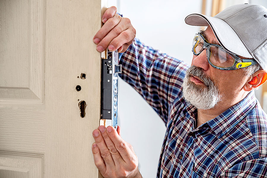 Door lock installation, repair, or replacement service. Door hardware installer locksmith working with open white door indoor.