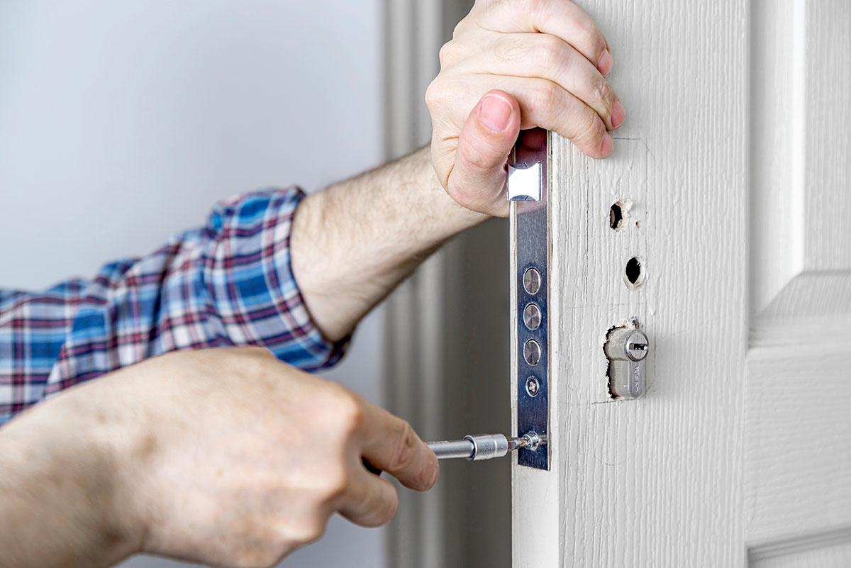 Door lock installation, repair, or replacement service. Door hardware installer locksmith working with open white door indoor. Hands of the master close-up