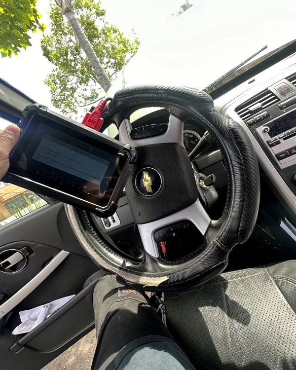 A Locksmith Long Beach technician holds a key programming tablet inside a Chevrolet vehicle while programming a new key