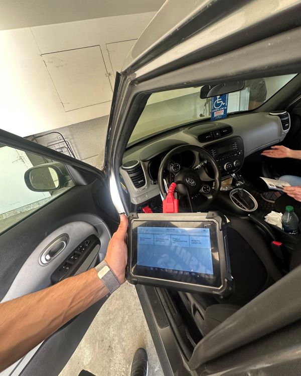 A car key programmer connected to a Kia vehicle during key programming.